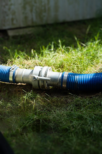 Čistá modrá hadice na zeleném trávníku, odvadějící vyhloubený materiál s vodou mimo pozemek.