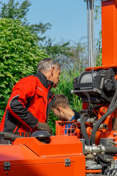 Muž v čerevné bundě REVER CZ stojící u vrtného stroje při vrtání studny kotroluje průběh vrtu pro vrtanou studnu.