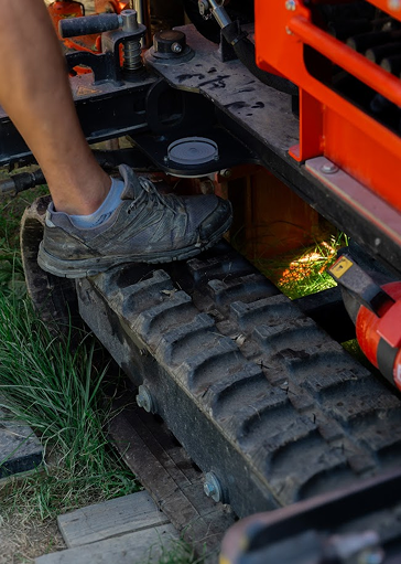 Malý pás šetrné vrtné soupravy společnosti REVER CZ stojící na zeleném osazeném trávníku, na kterém stojí noha studnaře.