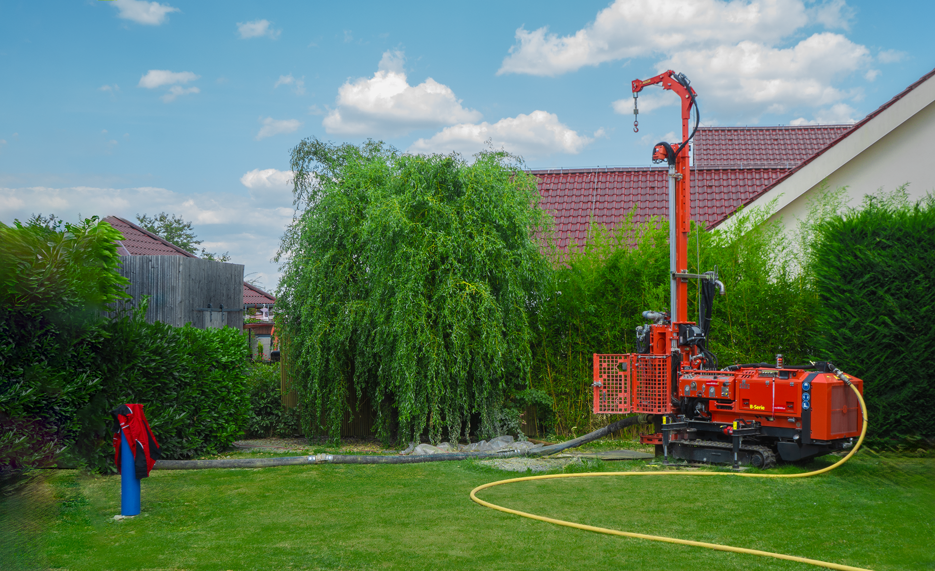 Červená vrtná souprava společnosti REVER CZ šetrně vrtající studnu uprostřed zelené, čisté, čerstvě osazené zahrady.
