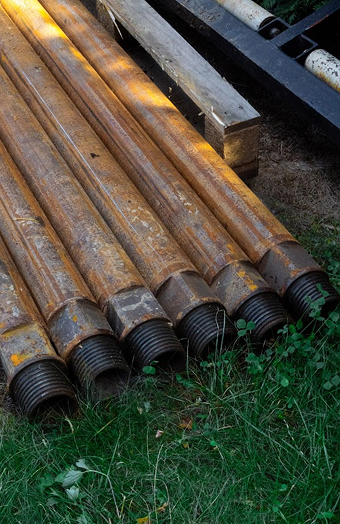Ocelové vrtné tyče srovnané a připravené na vrtání studny nebo vrtu pro tepelné čerpadlo, na zeleném trávníku.