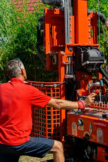 Muž v červeném tričku společnosti REVER.CZ obsluhuje malou a šetrnou vrtnou soupravu při prohlubování vrtané studny