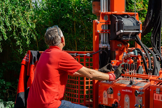 Muž v červeném tričku společnosti REVER.CZ obsluhuje malou a šetrnou vrtnou soupravu při vrtání studny na zahradě.